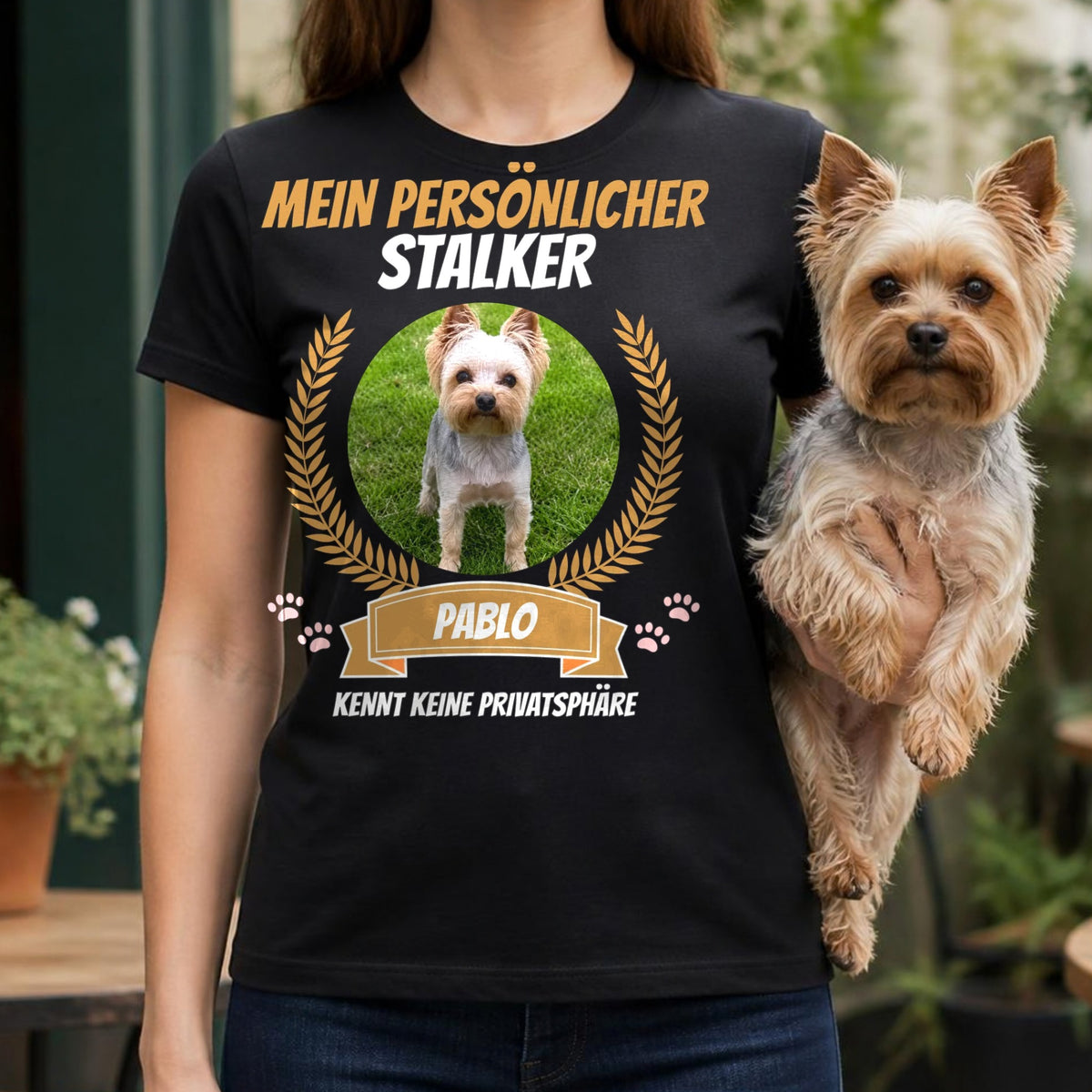 Frau traegt schwarzes T-Shirt Mein persoenlicher Stalker mit Yorkshire Terrier auf dem Arm auf Cafe-Terrasse